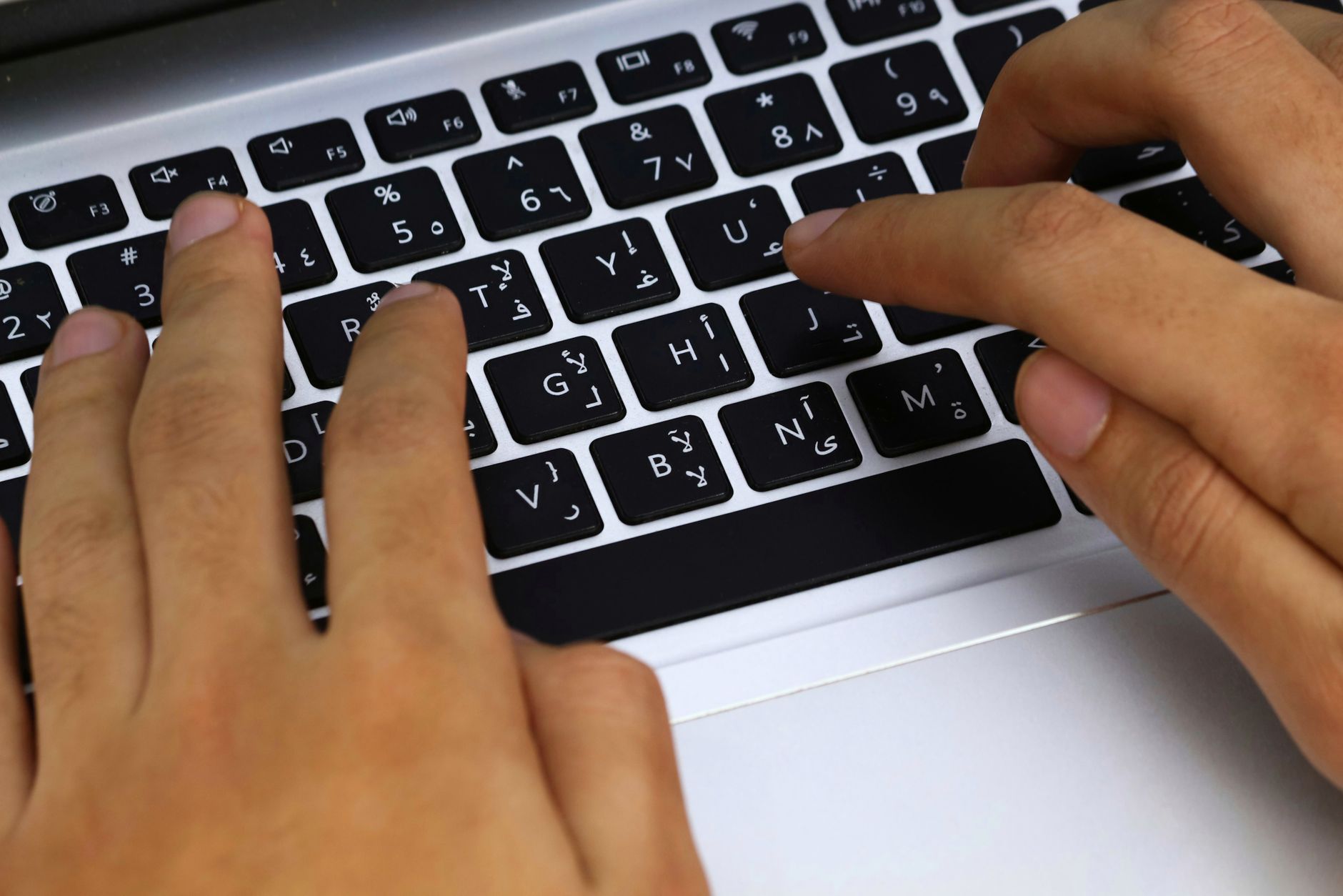 Close-up van handen die typen op een laptop met Arabisch toetsenbordlayout, waarbij moderne technologie in gebruik is.